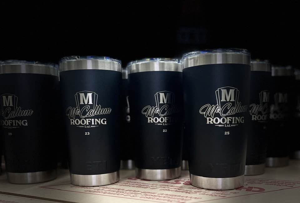 Row of dark blue insulated tumblers engraved with a McCullough Roofing logo
