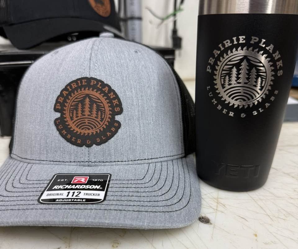 Matching grey snapback hat and black tumbler engraved with a Prairie Plains logo