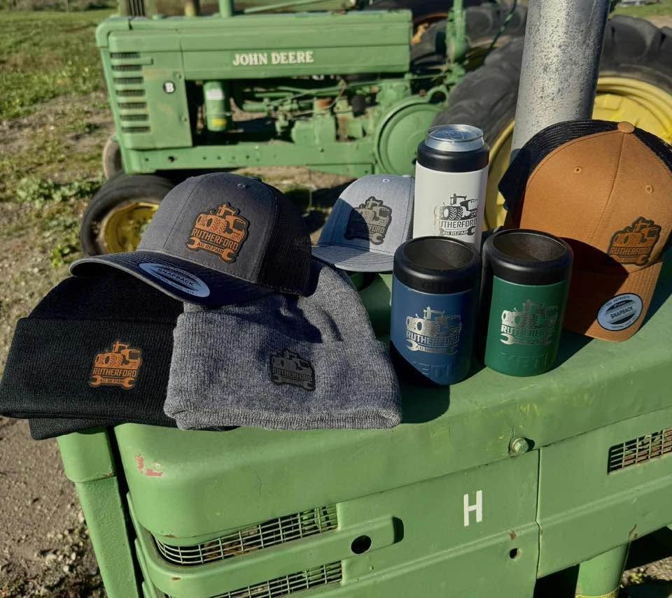 Custom hats and insulated bottles arranged on a green tractor hood outdoors